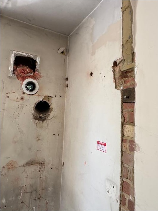 Internal wall with exposed service openings and removed finishes at the New Malden site.